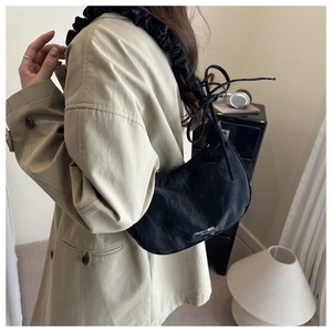 Detail of black pleated underarm bag with bow tie and logo worn with a trench coat