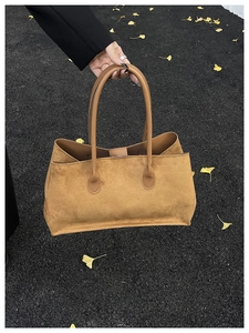 Brown suede tote bag with long handles held against autumn leaves on dark pavement