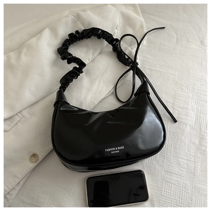 Detail of glossy black moon bag with ruched strap and FANYISSA text on white background