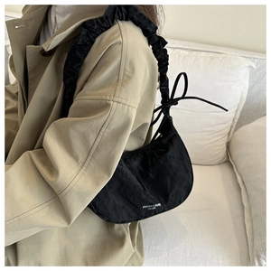 Detail of black crescent shoulder bag with ruffled strap and ribbon ties on a model