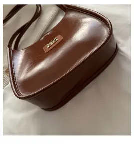 Detailed view of the brown glossy leather shoulder bag with gold logo and curved bottom base