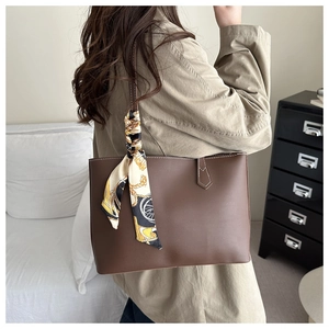 Brown leather tote bag featuring a decorative printed scarf on the handle in a home setting