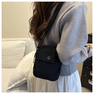 Close-up of black nylon crossbody bag with metal M logo shown on a person