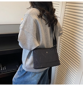 Détail du sac bandoulière en nylon noir avec texture en V et logo rond argenté