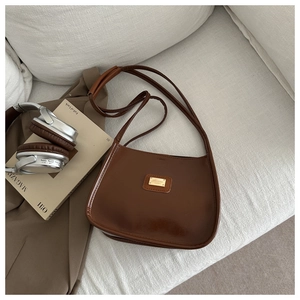 Detail of a brown vintage leather shoulder bag with gold metal logo on a soft sofa