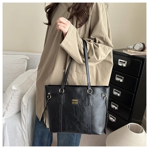 Detail of black pebbled tote bag with golden logo and decorative side drawstring accents
