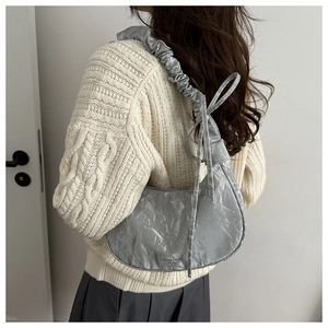Close-up of metallic silver crescent bag featuring bow detail and pleated shoulder strap