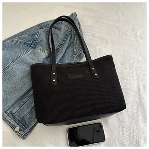 Detail of black corduroy tote bag with leather trim and rectangular brand logo patch
