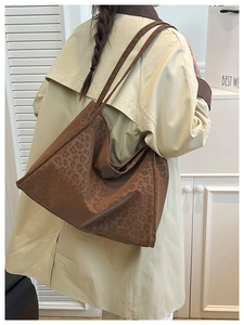 Side view of large leopard print tote bag styled with a beige trench coat indoors