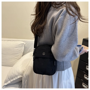 Close-up of black nylon crossbody bag with silver M buckle worn by a model