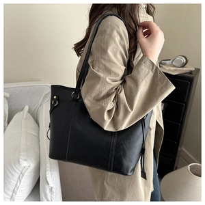 Side view of black tote bag with drawstring details and gold hardware on trench coat