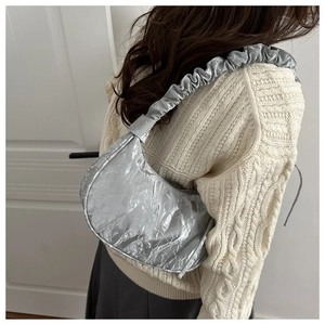 Detailed view of silver metallic pleated dumpling bag with ruched handle on shoulder