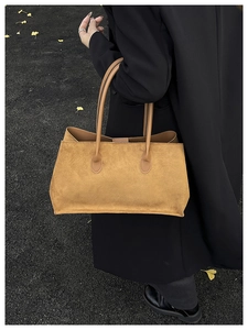 Outdoor shot of a matte camel tote bag paired with a black coat and autumn leaves