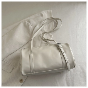 Detail view of a white vintage leather barrel bag on soft bedding showing textured surface