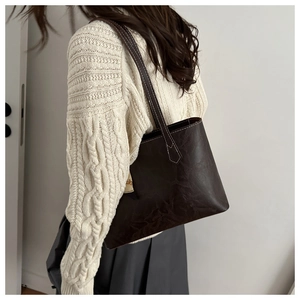 Détail d'un sac cabas marron foncé texturé porté avec un pull en maille et une jupe grise