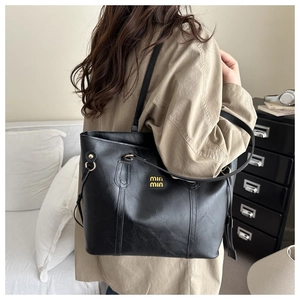 Detail of gold metal logo and drawstring texture on a black leather tote bag
