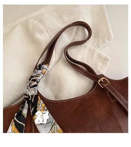 Detail of a brown leather shoulder bag featuring a patterned silk scarf and metal hardware