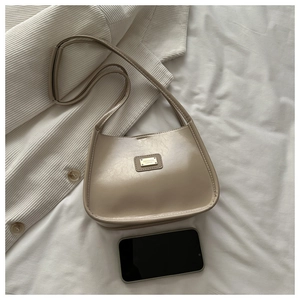 Detail of beige half-moon bag with gold metal logo and subtle faux leather texture