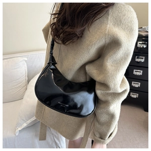 Close-up of black patent leather crescent shoulder bag featuring stylish white lettering