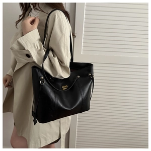 Detail of black textured leather tote with gold logo on a beige trench coat