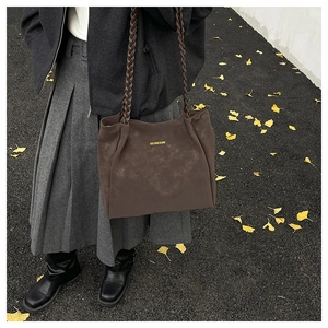 Detail of the brown suede tote bag with woven handles on a street with ginkgo leaves