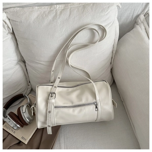 Detail of a creamy white cylindrical bowling bag with smooth leather and silver hardware
