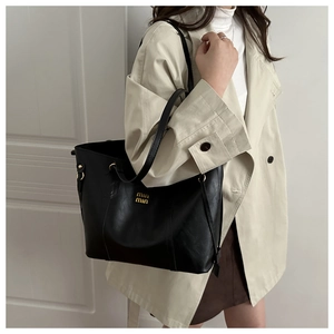 Detailed view of large black leather tote bag featuring gold metallic logo and shoulder strap