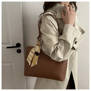 Detail of a brown leather tote bag with a patterned silk scarf on the shoulder strap