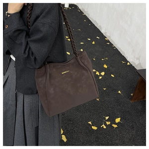 Detailed shot of dark brown tote bag featuring braided strap and gold logo lettering