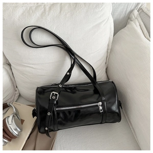 Detail of glossy black oil leather barrel bag with silver zippers and metal accents