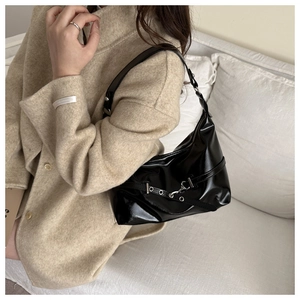 Detail of black glossy hobo bag with silver buckle and rivets worn over beige coat