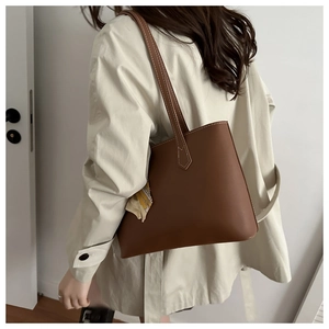 Brown leather tote bag detail with printed silk scarf accent on a beige trench coat
