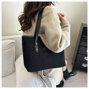 Detail of black corduroy tote bag showing vertical texture and sleek leather shoulder straps