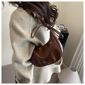 Detail of dark brown semi-circle underarm bag with glossy PU texture and pleated cloud strap
