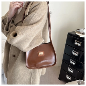 Detail of a brown leather shoulder bag with a vintage gold metal plate and long strap