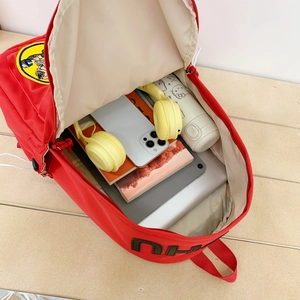 Large red school backpack with laptop compartment and cartoon patches on wooden desk