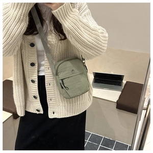 Detail view of light green crossbody bag featuring a zip front pocket and fabric strap