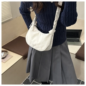 Close-up of white crescent crossbody bag featuring knotted strap and pleated texture
