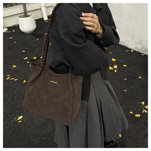 Detail of dark brown faux suede tote with braided strap and gold logo in outdoor setting