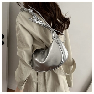 Close-up of metallic silver crescent bag with ruffled strap and tassel details on model