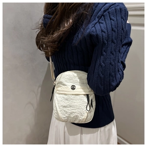 Detail of a beige pleated mini crossbody bag with metal logo on a navy knit sweater