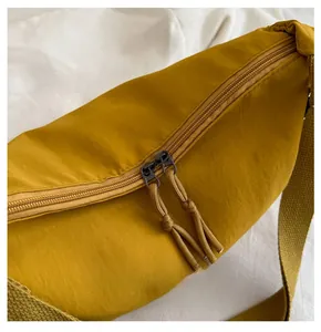 Detail view of smooth double zippers with woven pulls on a yellow nylon shoulder bag