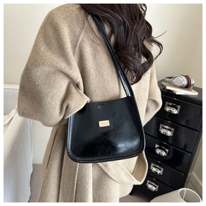 Detail of a black minimalist underarm bag in oily leather texture worn over a beige coat