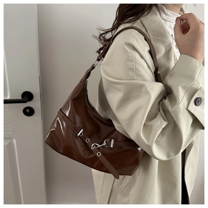 Dettaglio di una borsa a spalla in pelle verniciata marrone lucida con fibbia e anello