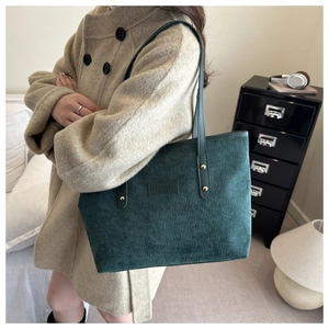 Detail of dark green corduroy tote bag with leather strap and metallic rivets on coat