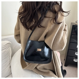 Detail of glossy black saddle bag with gold logo worn on a tan wool coat