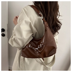 Close-up of brown faux leather hobo bag with silver buckle worn by a model in a trench coat