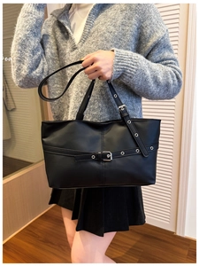 Detail of black PU tote bag with silver eyelets and buckle worn with grey sweater