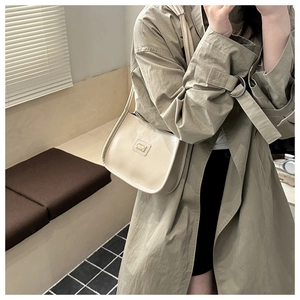 Detail of a beige half-moon hobo bag with gold hardware worn by a model in soft indoor light