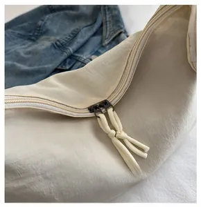 Close-up of dual metal zippers with woven pullers on an ivory nylon crossbody bag